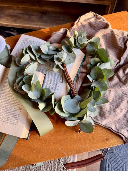 a small, heart-shaped decoration made from thin, pale birch branches that have been bent and woven together to form the outline. The wood looks natural and slightly textured, not polished
